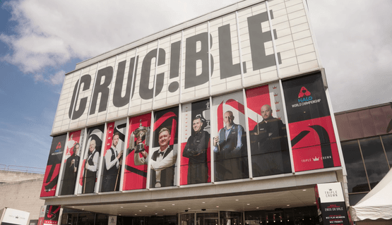 The front of the Crucible theatre in the sunshine. Vinyl posters of snooker players cover the windows