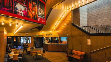 Image shows Crucible Kitchen situated in the lower foyer of the Crucible. A bar, tables and seating are visible in the image.