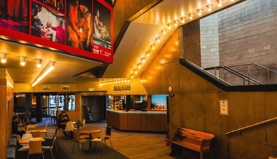 Image shows Crucible Kitchen situated in the lower foyer of the Crucible. A bar, tables and seating are visible in the image.