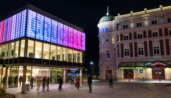 On the left, the Crucible lit up at night in purple and pink. Customers swarm through the doors. The Lyceum on the right, up-lit.