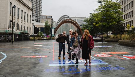 People laugh as they walk down Tudor Square, following a brightly coloured race track. Behind, the Winter Gardens can be seen.