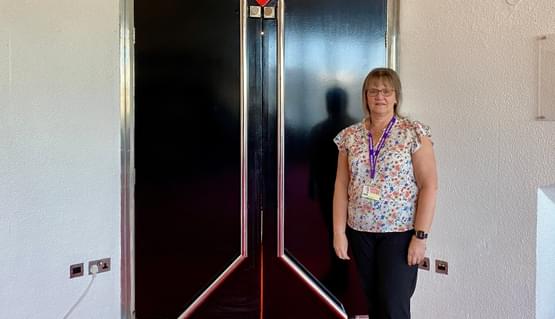 A person stands in front of a double door of a theatre auditorium. A large red arrow above the door points towards it