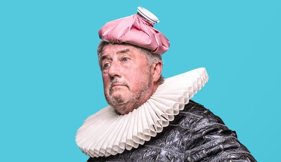 Promotional artwork for The Hypochondriac: A man wears 17th century clothing including a neck ruff, and holds a silk handkerchief. They wear an ice bag on their head as if it is a hat.