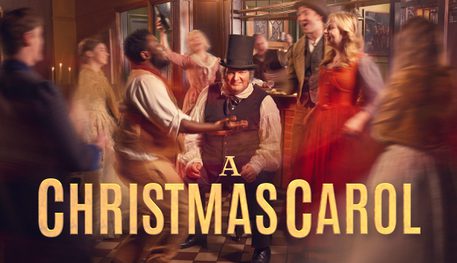 Promotional artwork for A Christmas Carol at the Crucible. Ebenezer Scrooge sits in a warmly lit Victorian pub looking directly at the camera with a roguish smile. He is surrounded by men and women of different ages celebrating, raising their drinks and dancing.
