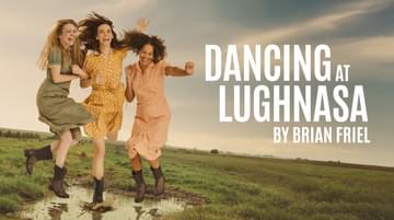 Three people with long hair and wearing pastel-coloured dresses smile and laugh as they hold hands and jump into a puddle in the middle of a grey green field. Text reads: DANCING AT LUGHNASA