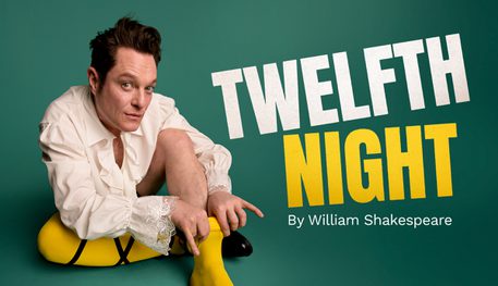 A person with black hair raises one eyebrow and smiles. They crouch down wearing a white blouse and daintily pull up a yellow stocking up their leg. Text reads: TWELFTH NIGHT