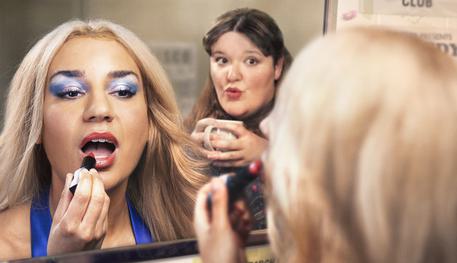 Two women reflected in the mirror in a 70s talent club dressing room. Julie on the left applies lipstick, Maureen on the right sips her tea.