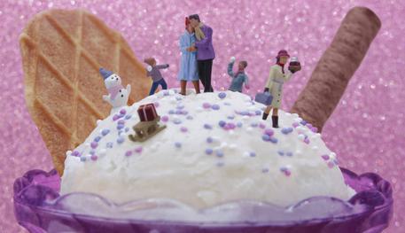 A snowy scene with small model people on an ice cream, a couple are surrounded by a snow man and kids chucking snow balls