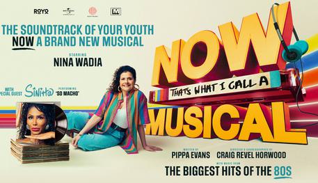 Promotional image for NOW That's What I Call A Musical with the title styled like the iconic NOW album covers with a pair of headphones hanging off the words. Nina Wadia sits leaning in front wearing a multi-coloured open shirt, white top and jeans. Pop star Sinitta can be seen on the cover of a vinyl record.