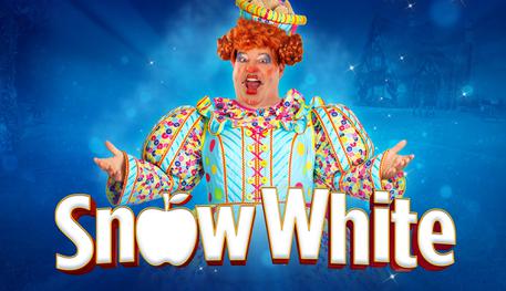 Promotional artwork for the 2024 Lyceum pantomime Snow White. Damian Williams as the dame in front of a blue background wearing a corseted dress covered in a multi-coloured button pattern. She opens her arms in a welcoming pose. Title reads Snow White in a white font with the letter O replaced with an apple.