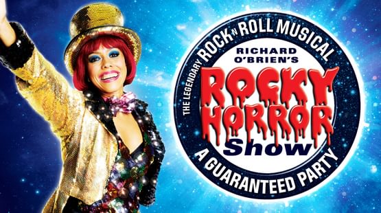 Promotional artwork featuring a woman with mid-length red hair wearing a gold sparkly jacket and top hat, sparkly top and bow tie with her arm raised in the air. The show title is written in dripping blood text. The tagline reads The Legendary Rock n Roll Musical and a guaranteed party.
