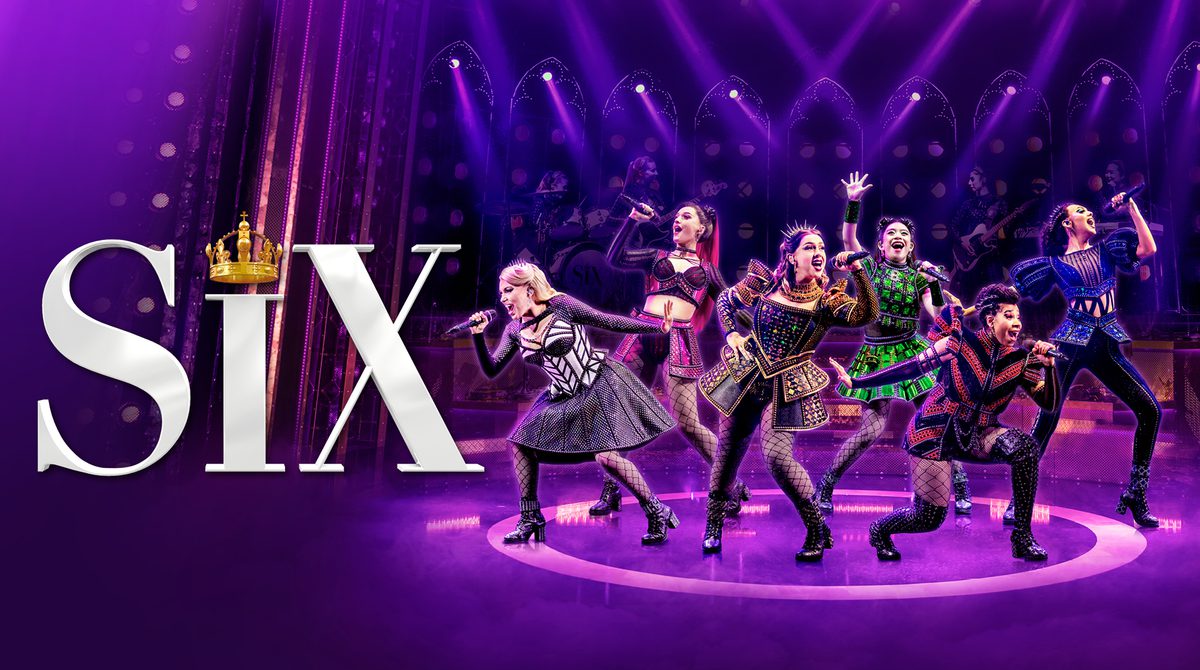 Promotional image for SIX featuring six young women as the six wives of Henry VIII stood on stage with purple lighting singing into microphones. They each wear a different colour on their modernised Tudor period costume.