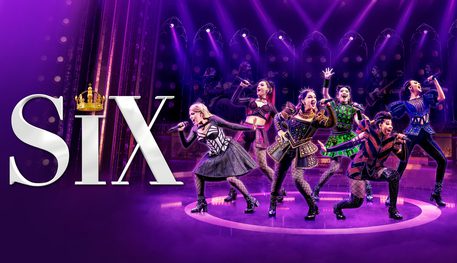 Promotional image for SIX featuring six young women as the six wives of Henry VIII stood on stage with purple lighting singing into microphones. They each wear a different colour on their modernised Tudor period costume.