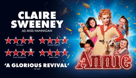 Promotional image for Annie featuring Claire Sweeney as Miss Hannigan holding a teddy bear by its ear and surrounded by four young girls and a dog.