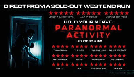 Promotional image for Paranormal Activity featuring a darkly lit room illuminated by a phone torch held by a man peaking through the gap in an open door.