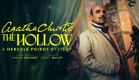 Promotional image for Agatha Christie's The Hollow. Featuring Peter Polycarpou as Hercule Poirot, a balding man with dark hair and moustache wears a creme suit with bow tie. He holds a walking cane in front of a window with a bullet hole breaking the glass.