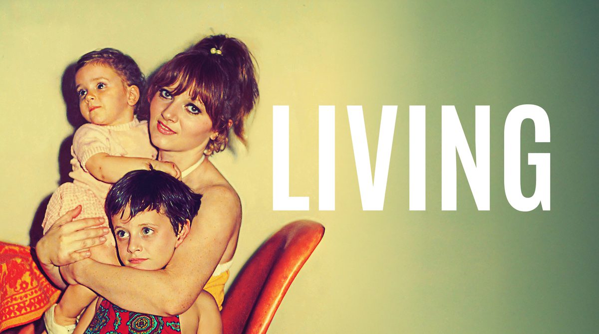 An old photograph of a young mother smiling, holding a toddler in one arm and hugging their other around a young child. They sit on an orange chair at a table. Text reads LIVING