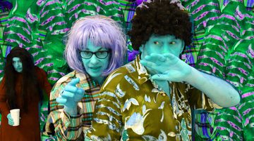 Promotional image for Cold Sweat featuring a man and woman with turquoise skin and contrasting hair colours. They wear colourful patterned shirts. Behind them, a woman with long black hair holds a cup. They stand against a green leafy background.