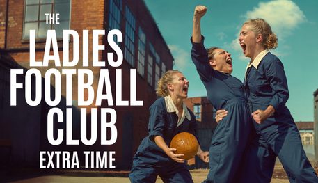 In the courtyard of a factory, three people wearing blue boilersuits scream with joy and triumph. One holds a brown leather ball, one punches the air and one grabs the other's waist. Text reads: THE LADIES FOOTBALL CLUB: EXTRA TIME