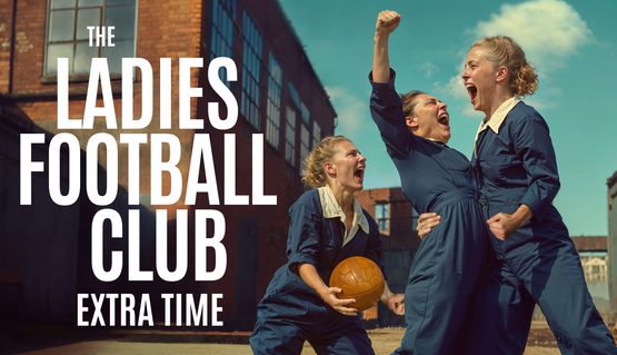 In the courtyard of a factory, three people wearing blue boilersuits scream with joy and triumph. One holds a brown leather ball, one punches the air and one grabs the other's waist. Text reads: THE LADIES FOOTBALL CLUB: EXTRA TIME