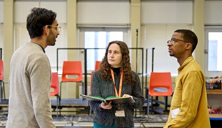 Three people are in conversation in a rehearsal room.