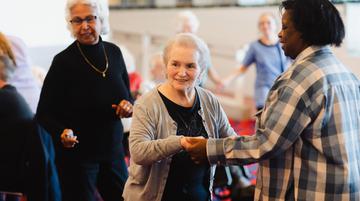 A Dementia Friendly Tea Dance at Sheffield Theatres. Photo by Becky Payne. Three older women smile and dance in the Crucible foyer.