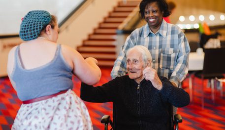 A Dementia Friendly Tea Dance at Sheffield Theatres. Photo by Becky Payne. An older man using a wheelchair cheers and smiles as a singer points to him.