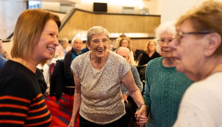 A group of older people smile and laugh together. One person looks at the camera, beaming