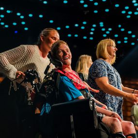 A person smiles as they are pushed forward in a wheelchair.