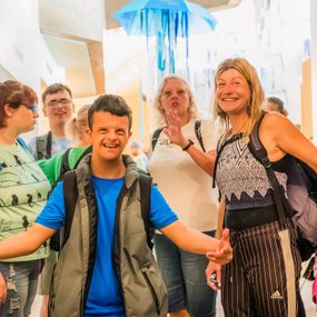 A group of people smile as they walk down a bright corridor. Above, a blue jellyfish art installation can be seen