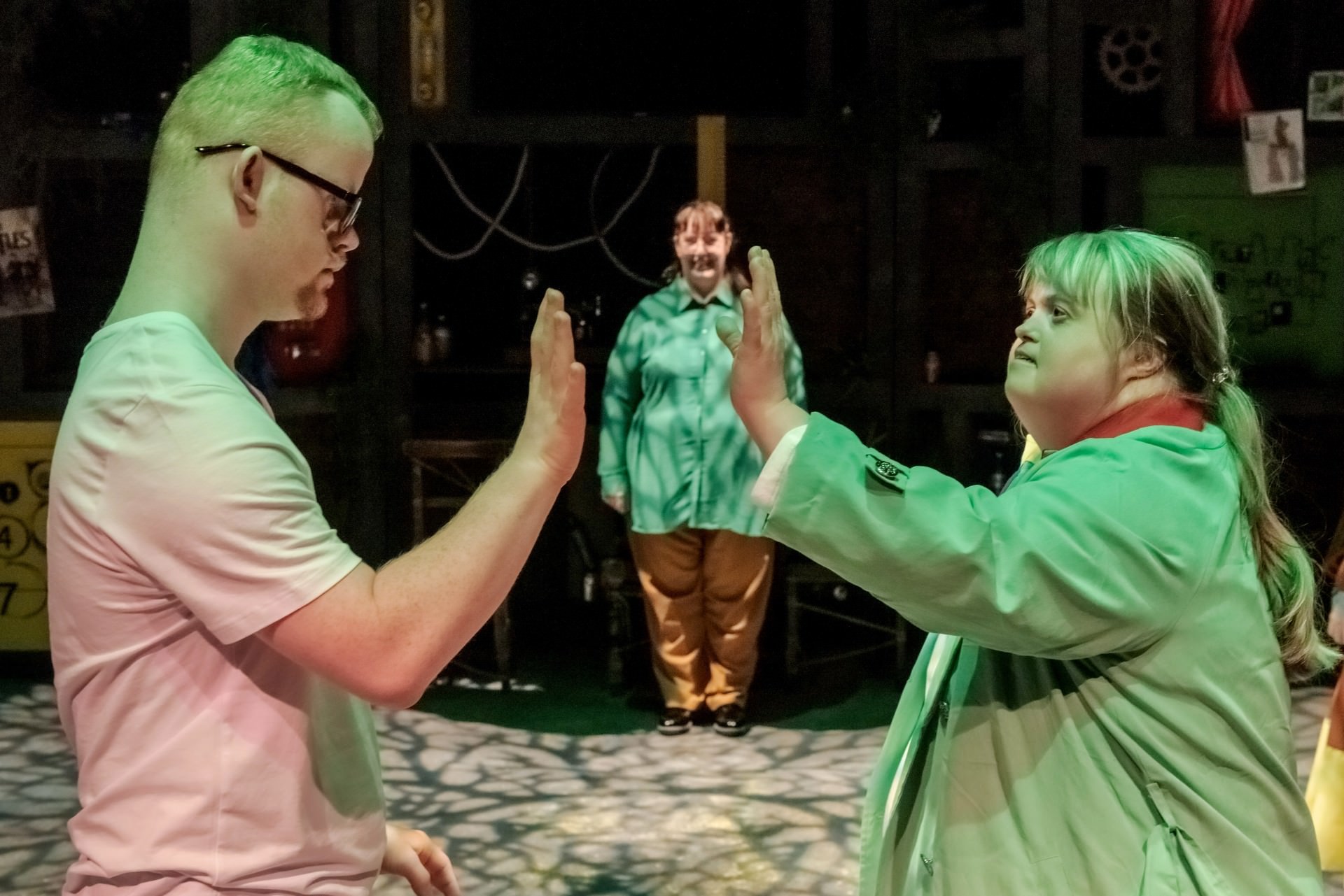 Production image of Communitree, from Launchpad our community theatre group for adults with learning disabilities. A man and woman high five and a woman stands in the background in the centre of their hands.