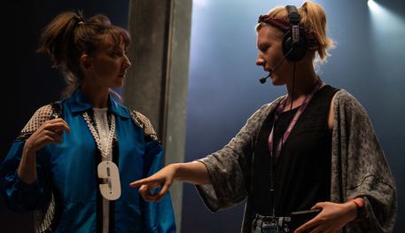 Backstage image featuring a female production manager with blonde hair wearing a headset with microphone while talking to a cast member