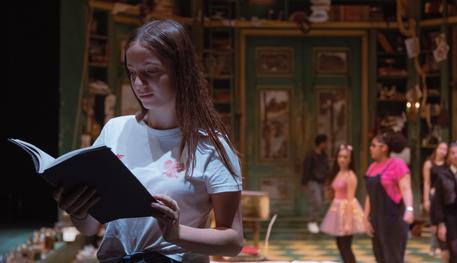 Three female students explore the set of The Hypochondriac, inspired by an 18th century estate. The girl in the foreground looks through a book.
