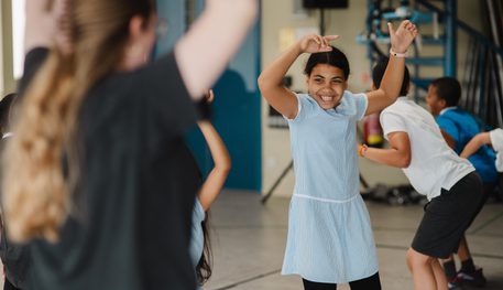 A group of young people laugh and dance in a rehearsal room.