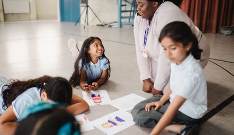 Young people sit on the floor working on colouring in sheets. One smiles up at an adult sitting with them