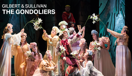 Text reads: 'Gilbert & Sullivan The Gondoliers'. The cast of The Gondoliers are performing on stage. They are wearing pale flowy dresses and holding up flowers.