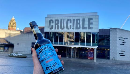 The Crucible theatre with a hand holding a bottle of Henderson's relish in front of it.