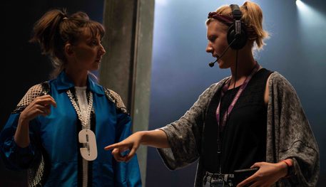 A production manager wearing a headset directs and actor dressed in blue