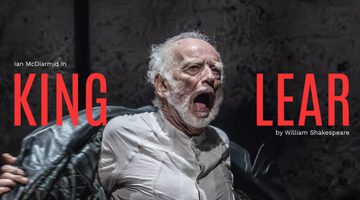 Ian McDiarmid (King Lear) in King Lear. Photo by Johan Persson. An older person with a white beard wears a long leather coat and shouts, ripping off their coat.