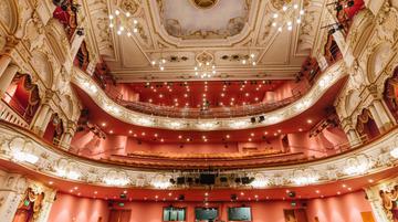 The interior of the Lyceum theatre. A traditional Victorian theatre looking up at the seats. Chandeliers hang from the ceiling and warm orange seating and walls hug the space.