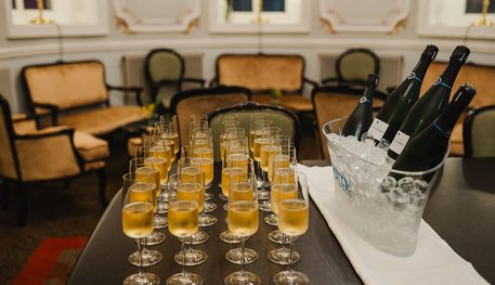 Image of the Macdonald Room with filled champagne glasses lined up on a table and bottles in a bucket of ice. The ornate furnished room can be used as a private bar and meeting space for events.