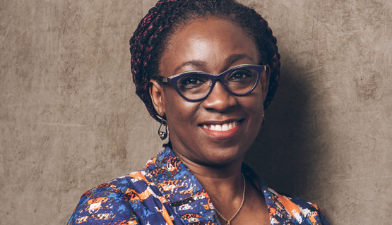 Bookey Oshin wears a brightly patterned top and glasses smiles.