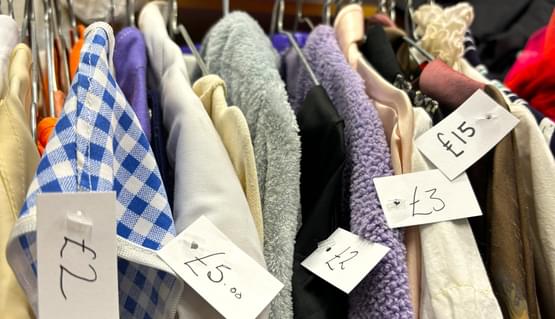 A rail of colourful clothing on hangers with labels stating the prices.