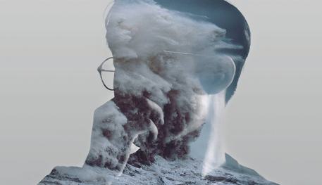 The profile of a person with glasses facing to the side against a grey background. Their outline is filling with crashing waves of the sea.