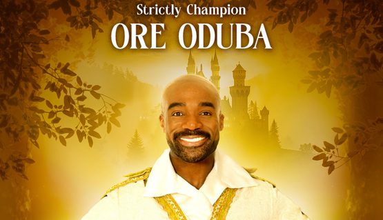 A person with a beard smiles and holds their hands on their hips, wearing a white and gold shirt. Text reads: STRICTLY CHAMPION ORE ODUBA