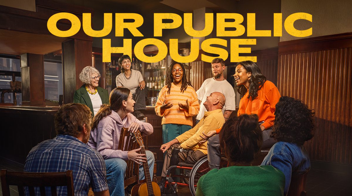 Text reads: 'Our Public House'. There are ten people of mixed ages in a pub. There is a woman in the centre who is talking and everyone is watching her and smiling. One woman is holding a guitar.