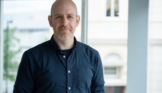 A portrait of a young white man wearing a dark blue shirt and smiling.