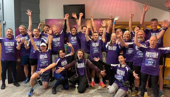A group of people wearing purple t-shirts shout and smile with their hands held up in the air.