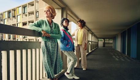 Three women lean against a concrete balcony overlooking Park Hill flats in Sheffield.