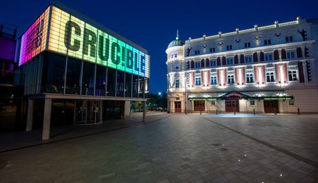 The Crucible and Lyceum theatres at night. The Crucible is lit up in rainbow lights, the Lyceum is lit up in white light.